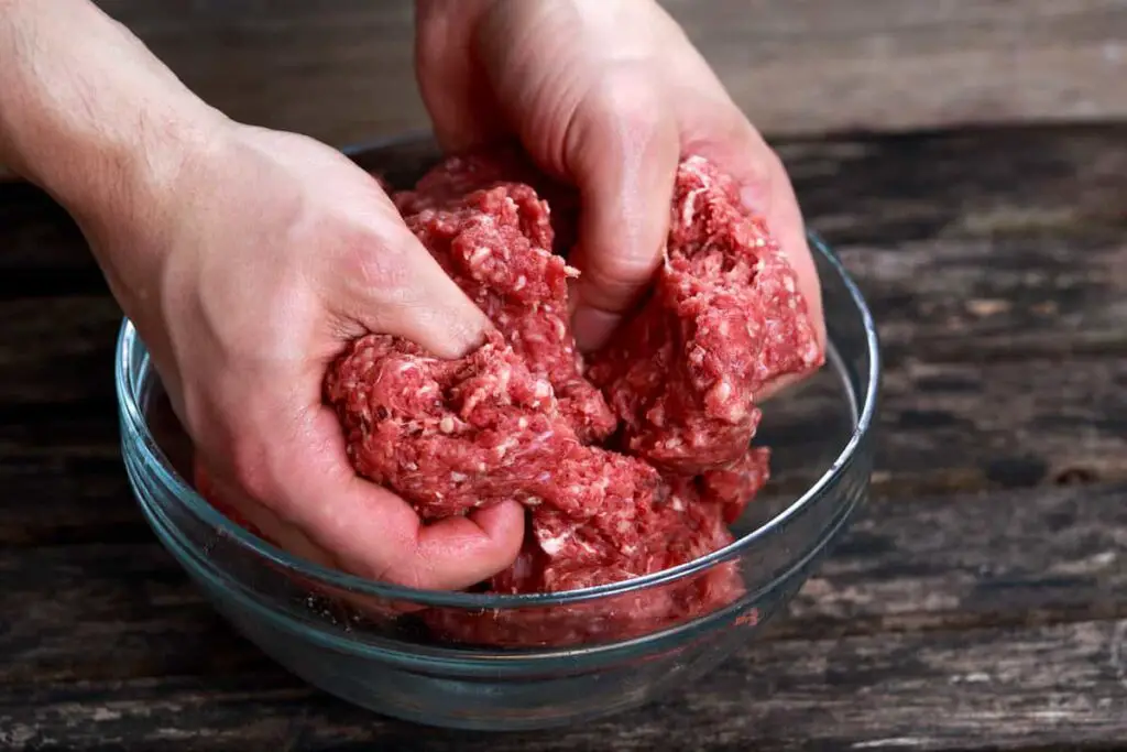 A man working ground beef with his hands.