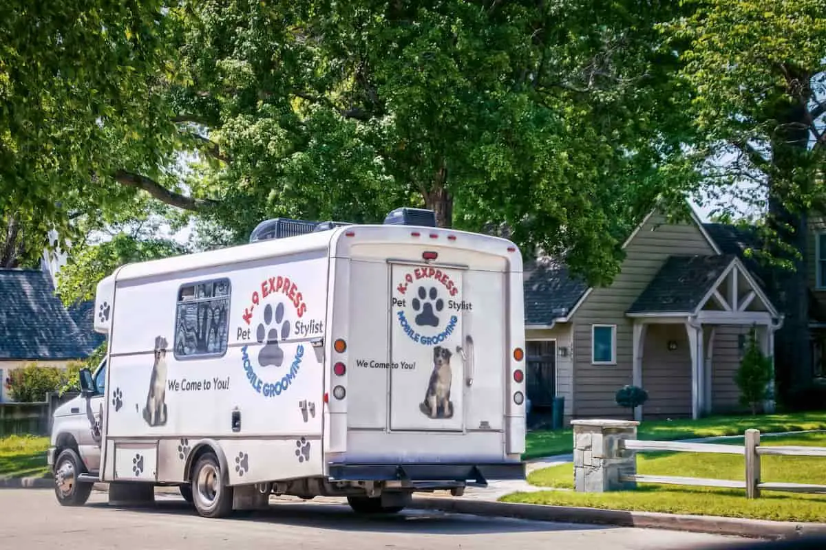 A mobile dog grooming van outside a home.|