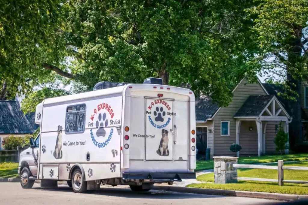 A mobile dog grooming services van outside a home.